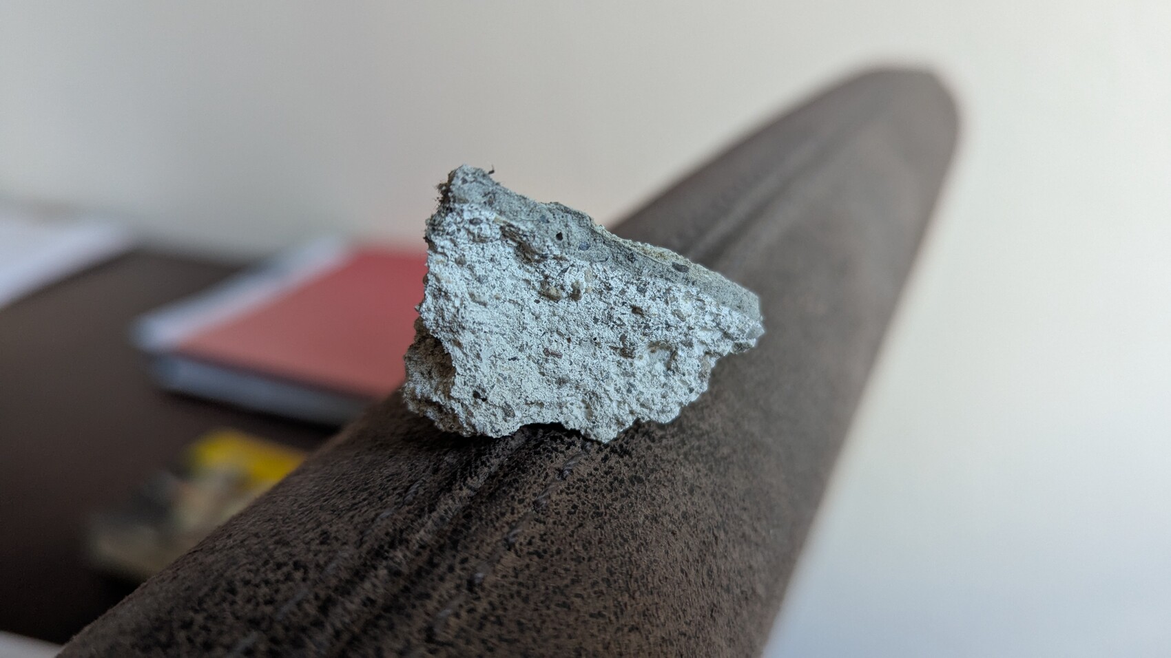 Grauer Betonbrocken liegt auf dem Polsterarm eines dunklen Sofas; unscharfer Hintergrund.