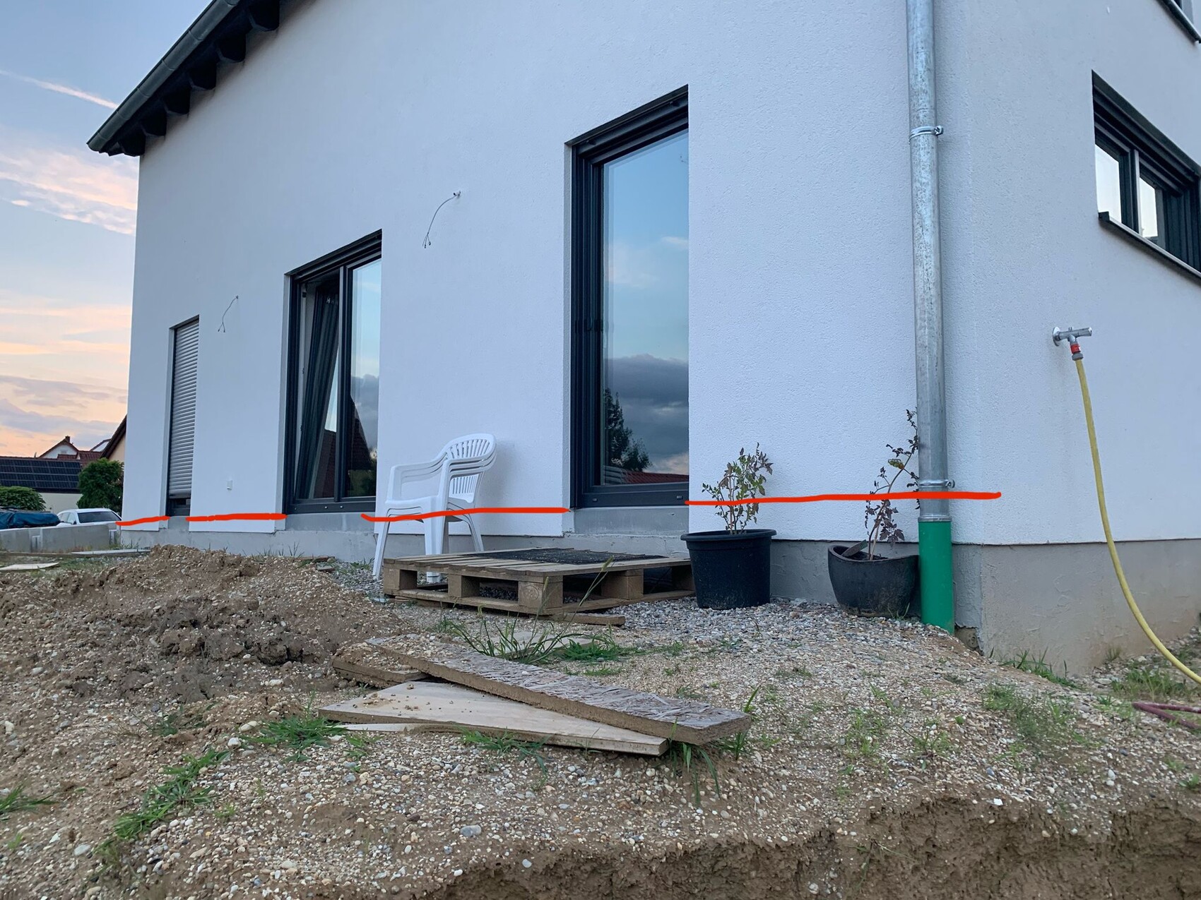 Außenansicht eines modernen Hauses mit Terrassenbereich, Pflanzkübeln und Baugrund