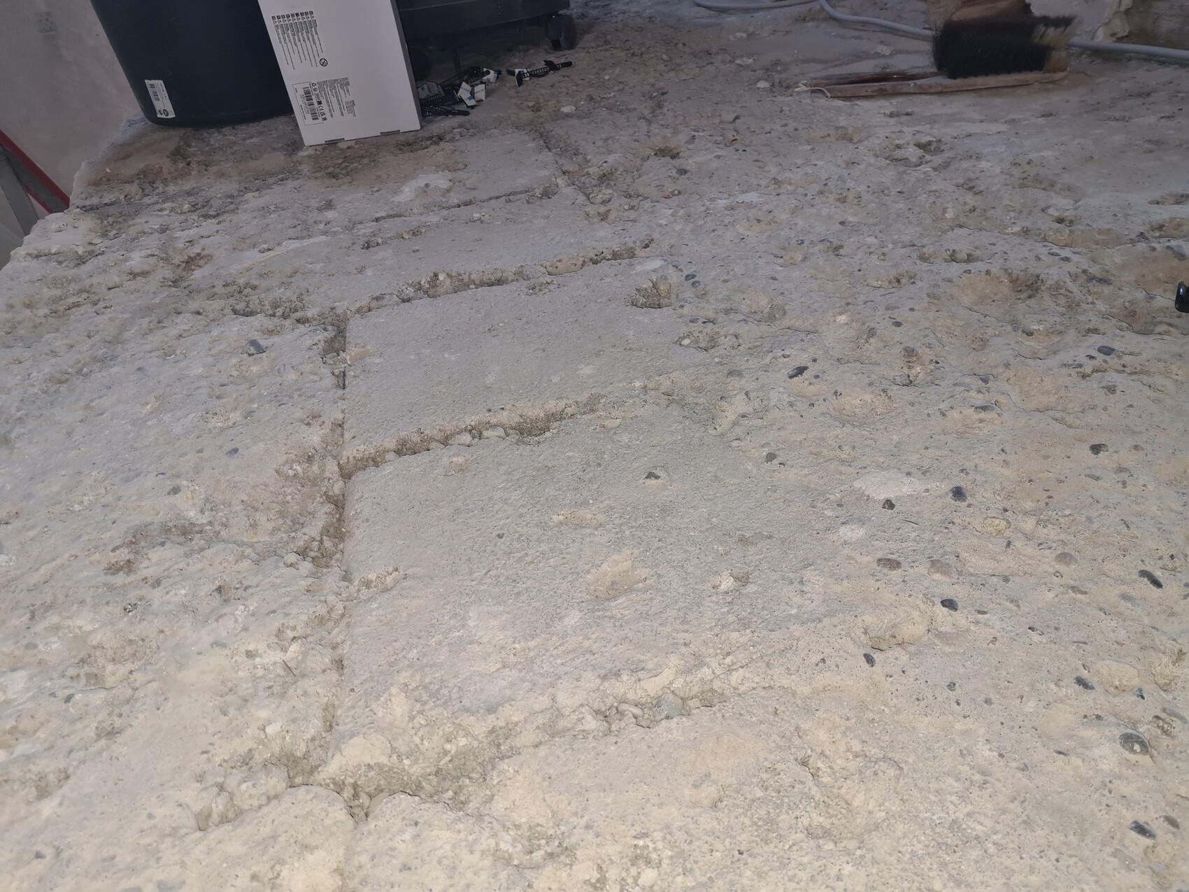 Rauer Baustellenbetonboden mit zwei rechteckigen Platten, Kies und Schutt.