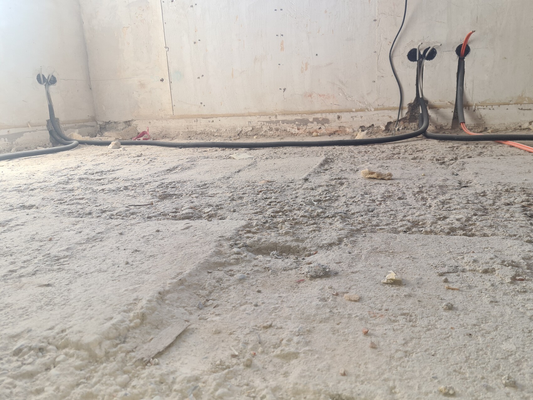 Baustelle: Unverputzte Wände, offene Kabel und Rohre, Kabelschläuche am Boden, Staub.