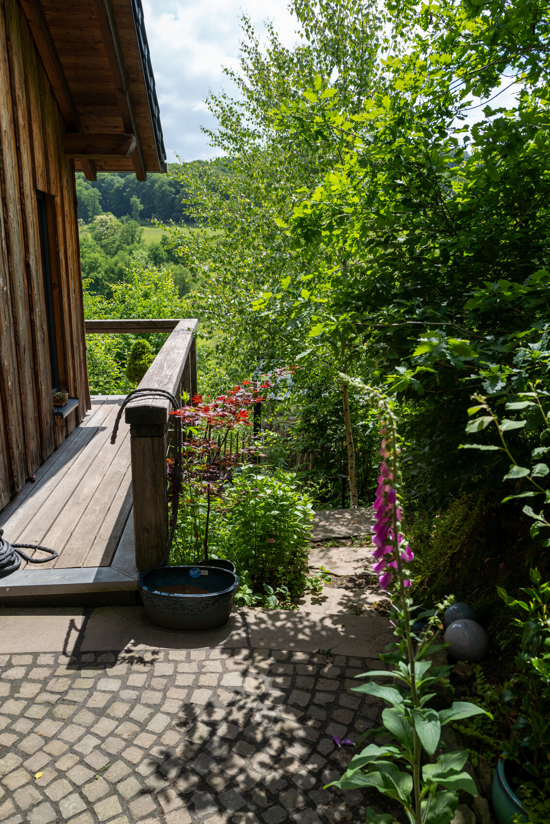 Außenansicht eines Holzhauses mit Veranda, Treppenstufen und umliegenden Bäumen