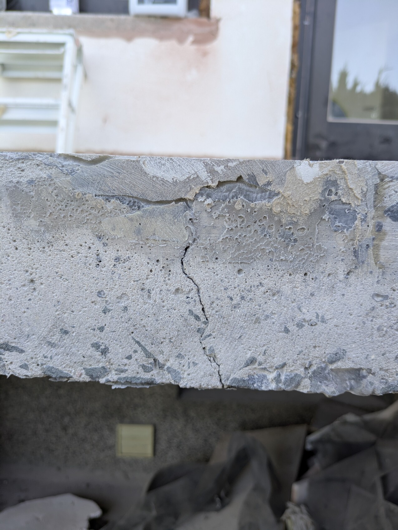 Nahaufnahme einer rauen Betonplatte mit Riss, Hintergrund: Gebäude mit Fenster.