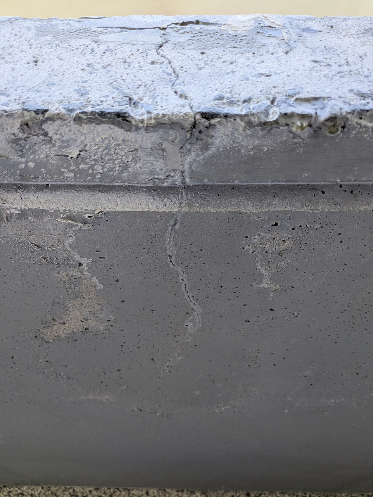 Nahaufnahme einer Betonwand mit vertikalem Riss und rauer Oberkante.