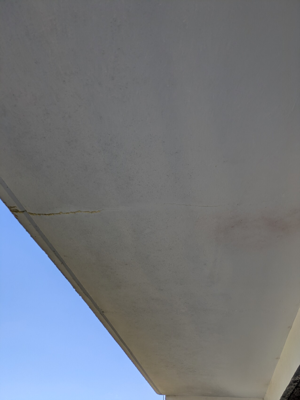 Unterseite eines Betonbalkons mit Riss, blauer Himmel im Hintergrund.