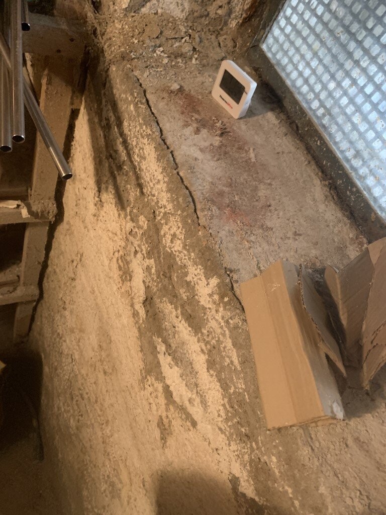 Staubiger Kellerboden; weiße digitale Anzeige (Sensor) steht auf dem Boden, Kartonreste daneben.