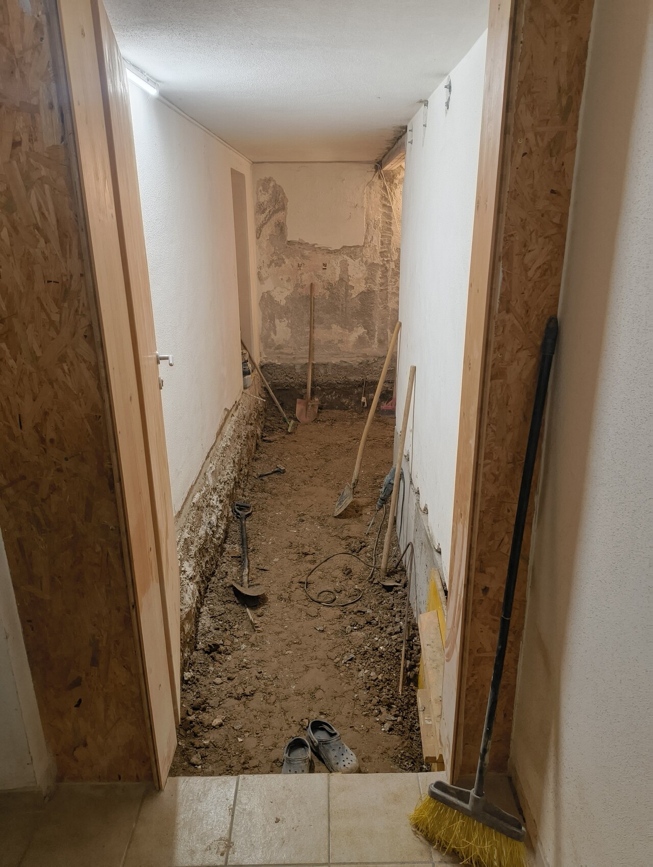 Korridor im Umbau mit offener Erdfläche, Schaufeln und Besen als Werkzeuge.