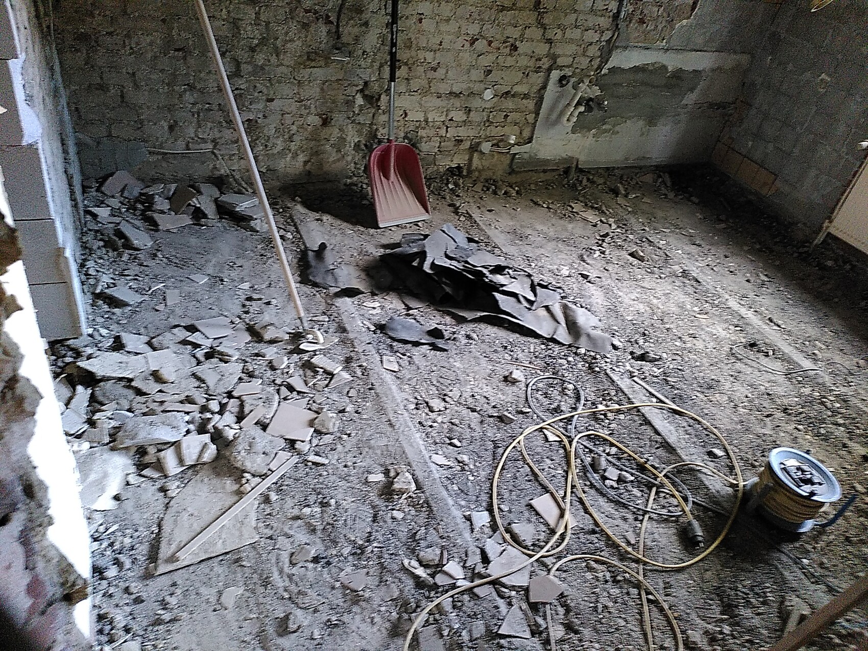 Baustelle im Innenraum mit Schutt, Schaufel und Kabeln, unfertige Wände.