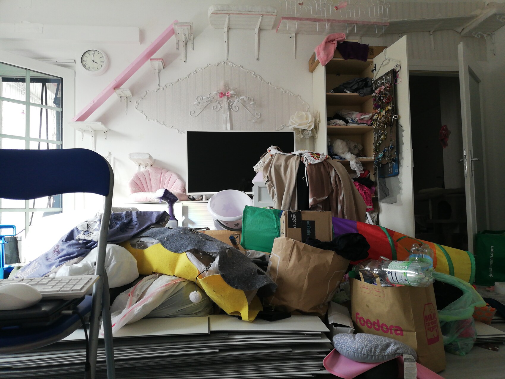 Chaotisches Wohnzimmer mit Kleidung, Kartons und Fernseher.