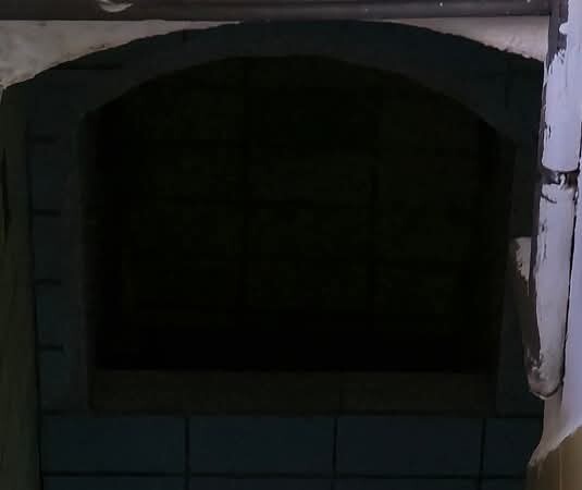 Dunkler Ofen mit bogenförmiger Öffnung und Fliesenboden im Küchenbereich.