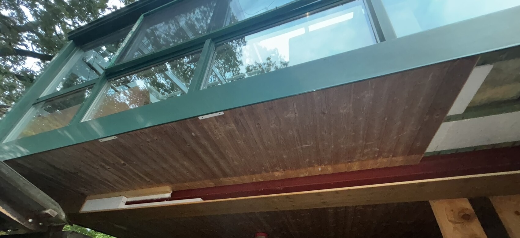 Moderne Terrassenkonstruktion mit Glasgeländern, grünem Metallrahmen und Holzboden