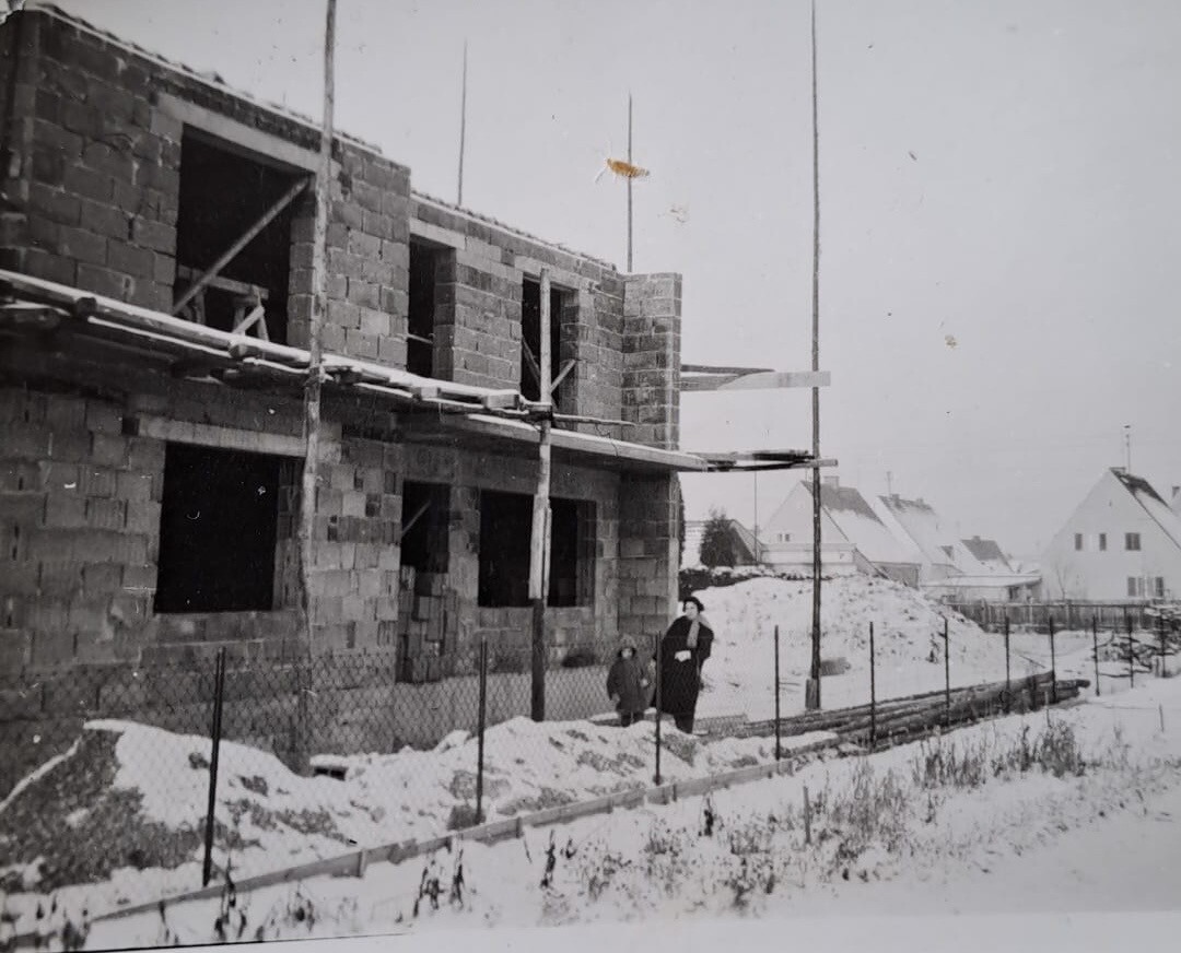 Schwarz-Weiß-Aufnahme eines unfertigen Rohbaus mit Gerüst und verschneiter Baustelle.