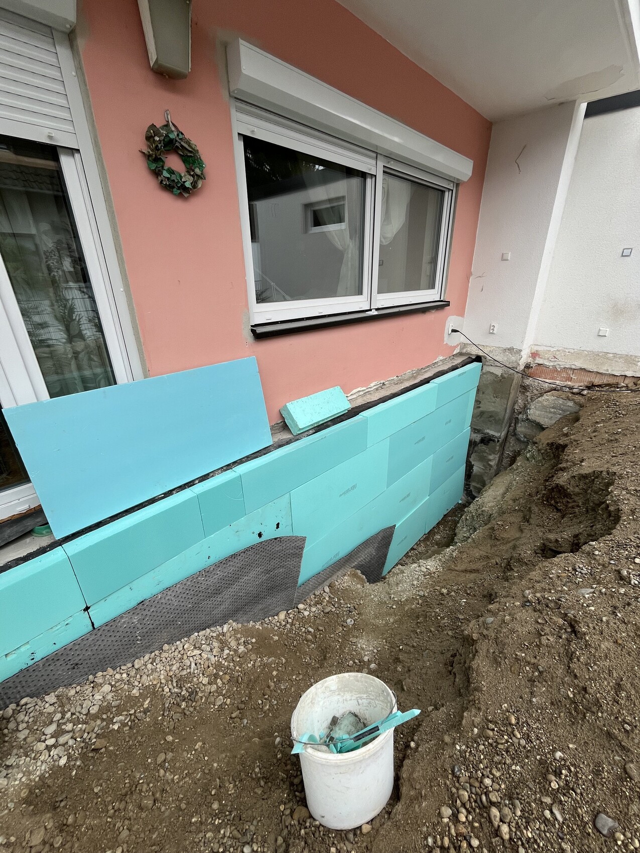 Außenwand mit blauen Dämmplatten, Baugrube, Eimer vor Hausfassade