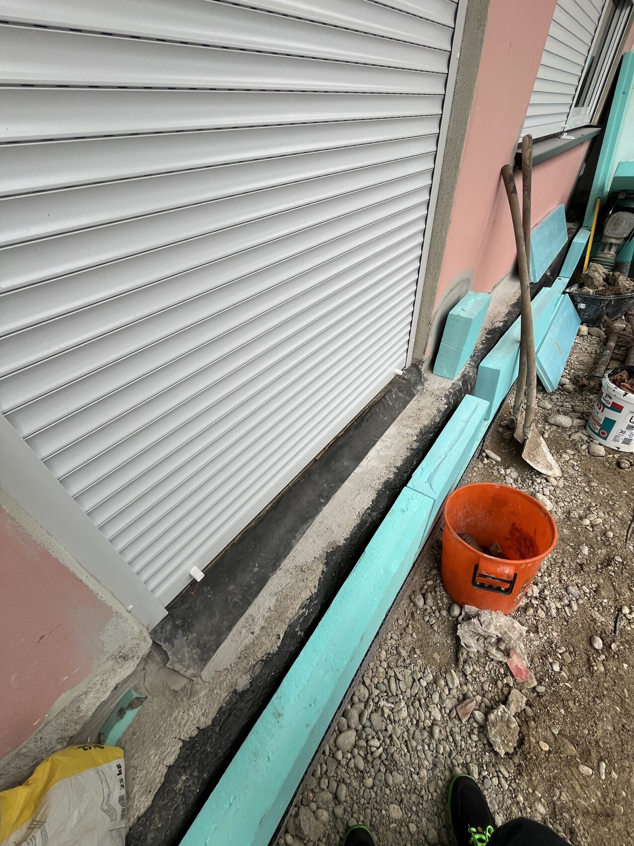 Außenbaustelle am Haus mit Rollladen, Bauwerkstoffen und Eimer