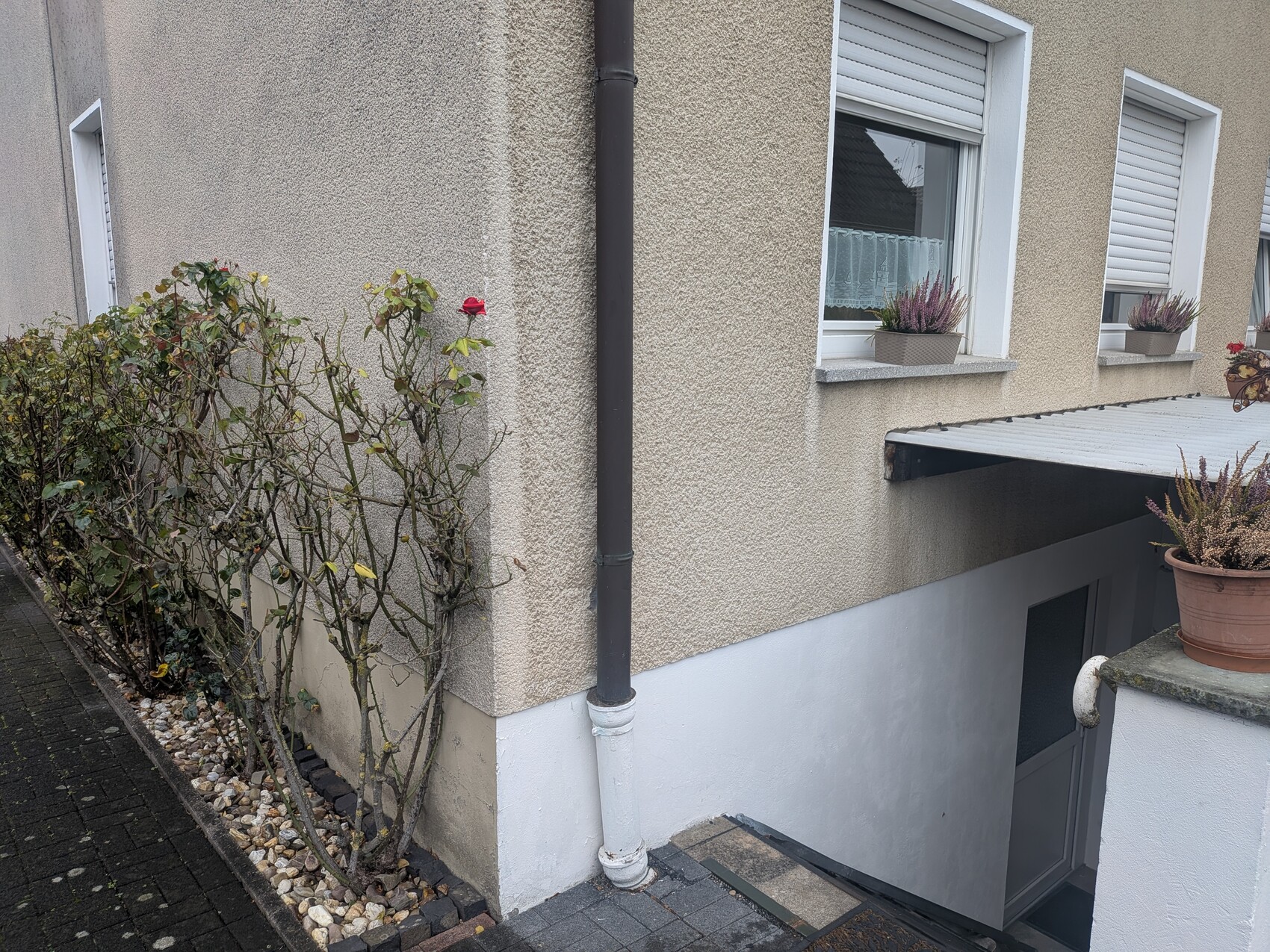 Außenansicht eines beigefarbenen Hauses mit Fenstern und Pflanzkübeln.