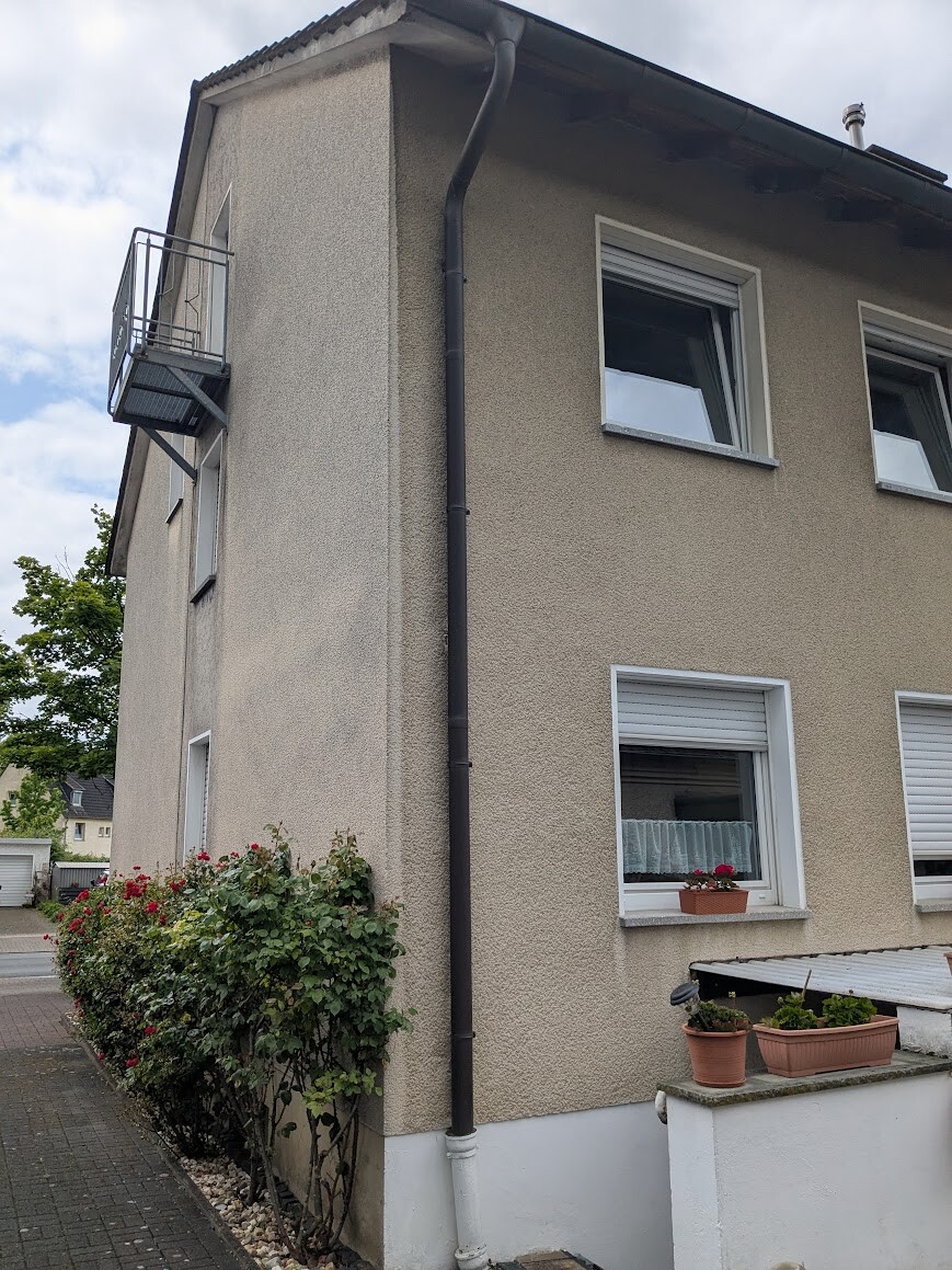 Außenansicht eines zweigeschossigen beige verputzten Hauses mit Balkon und Pflanzkübeln.