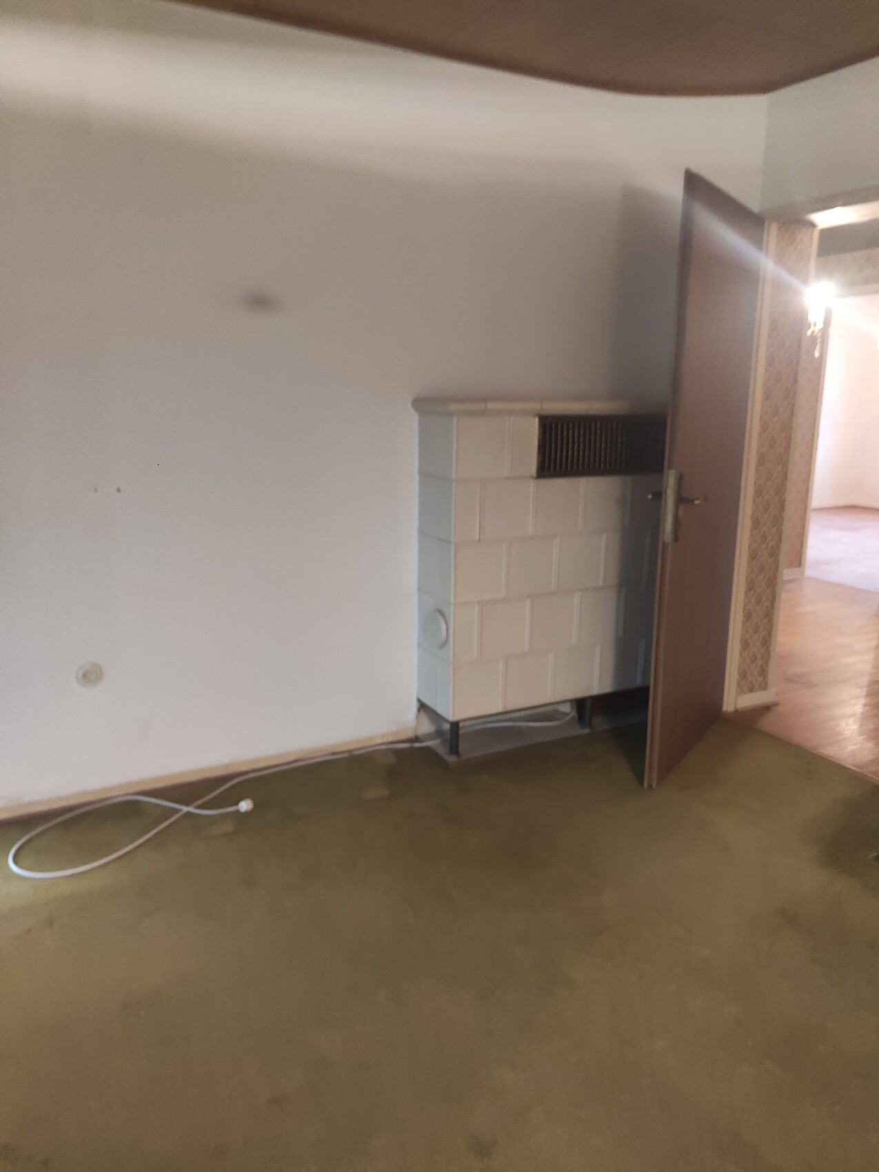 Alter weißer Kachelofen an der Wand, freistehend, Tür geöffnet, Kabel auf dem Boden