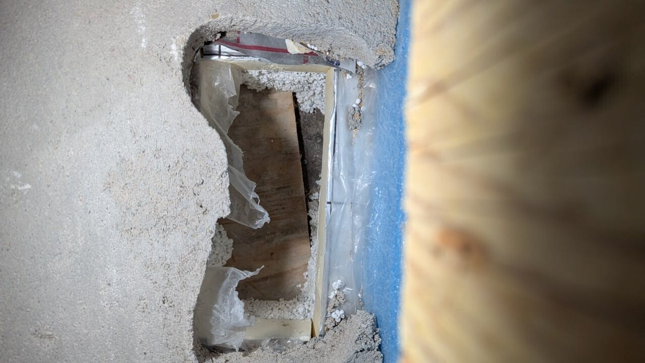 Angerissene Innenwand mit Staub, Dämmung und Plastikfolie während Renovierungsarbeiten