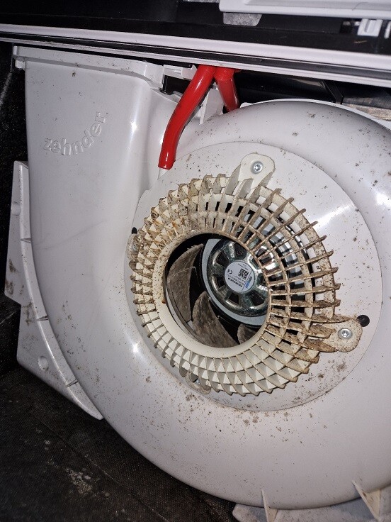 Runder Lüfter im weißen Haustechnik-Gehäuse mit Staub und rotem Kabel