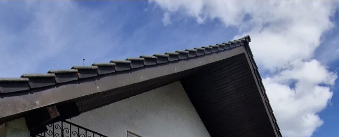 Dachkante eines Hauses mit dunklen Dachziegeln vor blauem Himmel