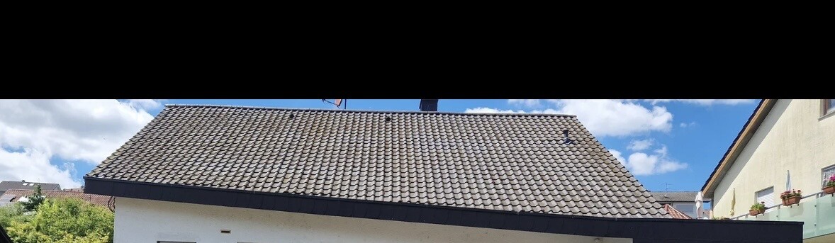 Hausdach mit Ziegeln, helle Fassade und blauer Himmel im Hintergrund