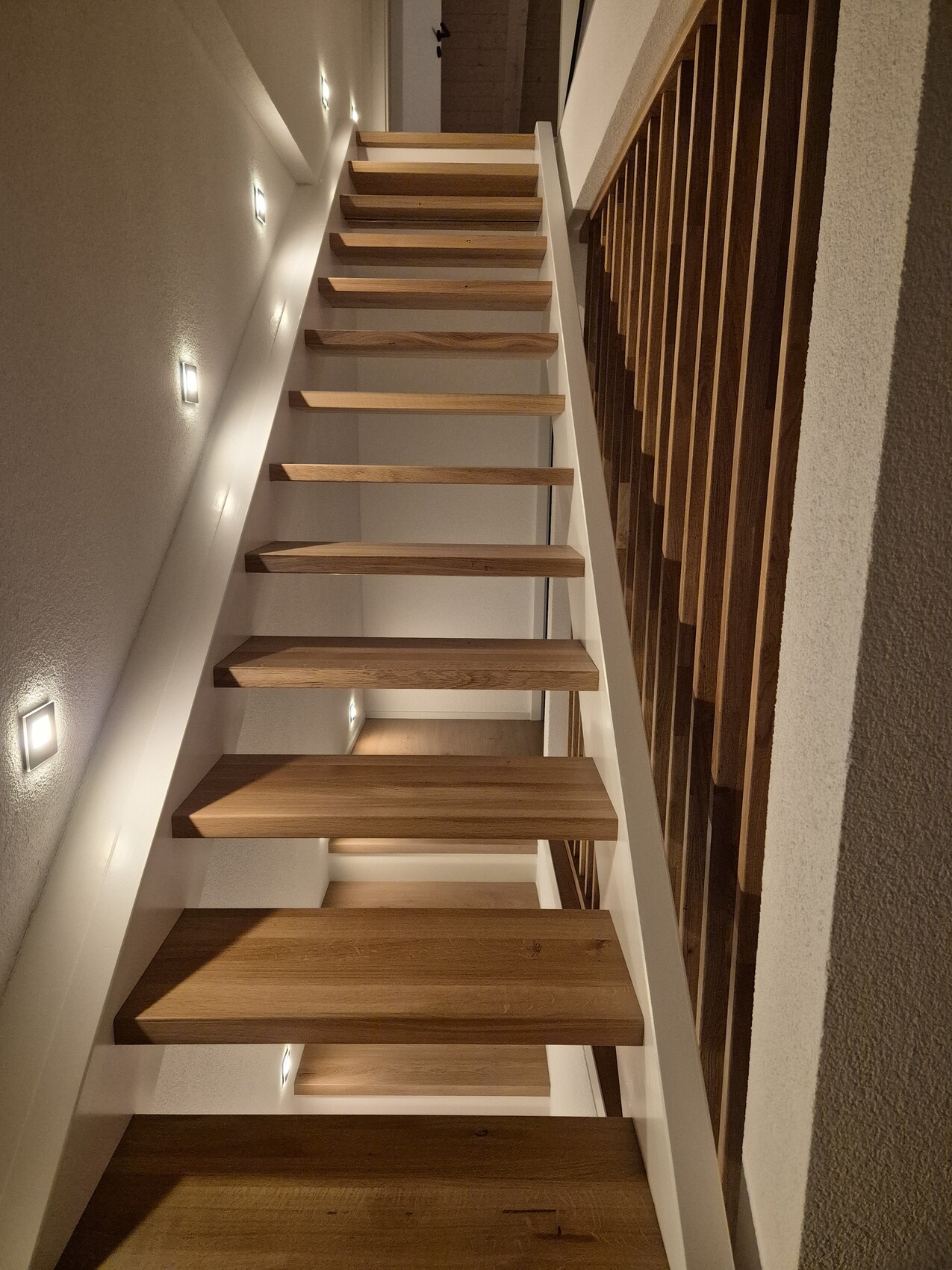 Moderne Holztreppe mit Geländer in hellem Innenflur eines Hauses.