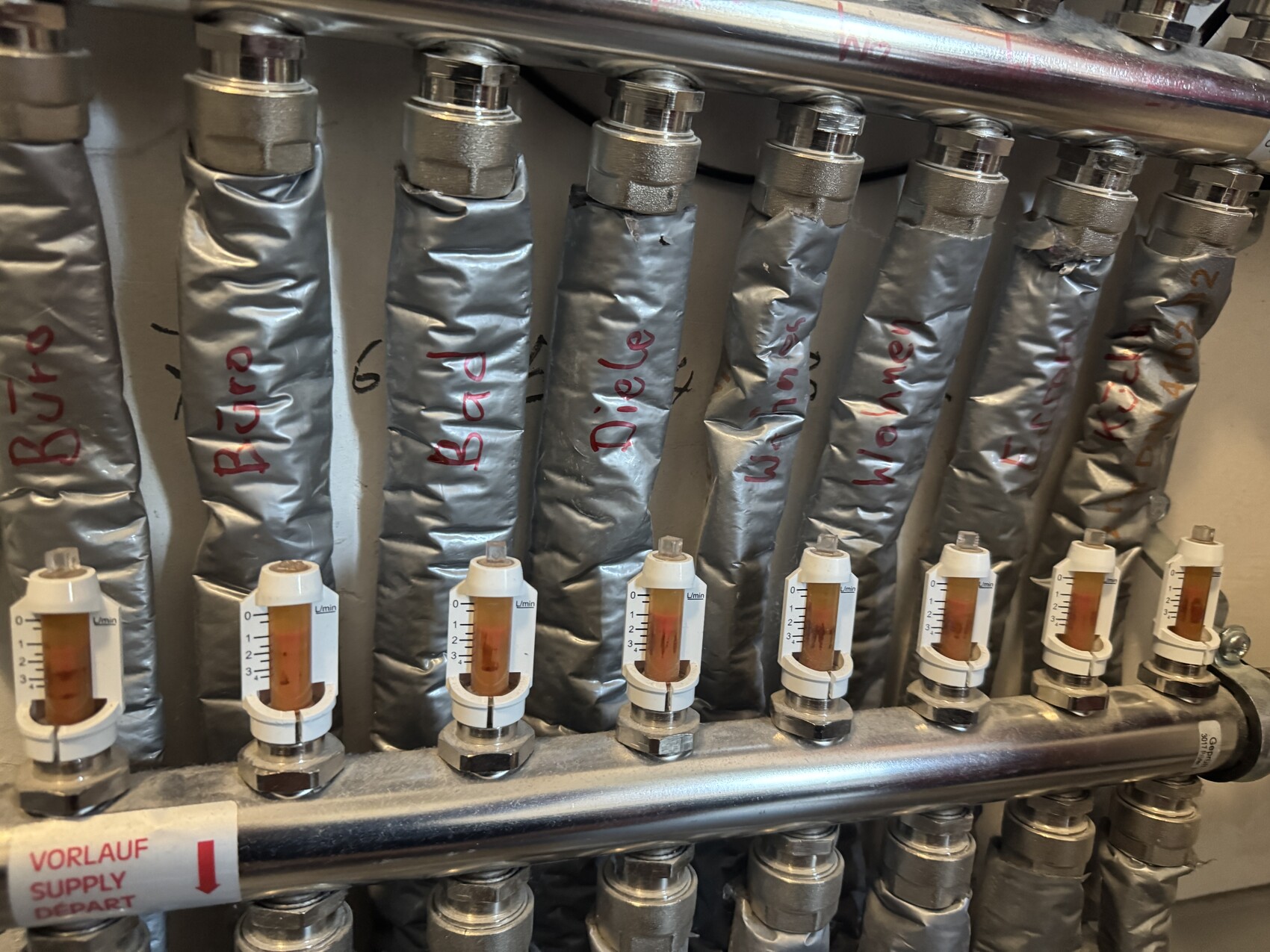 Isolierte Heizungsrohre mit Durchflussmessern in einer Heizungsanlage, sichtbare Ventile.