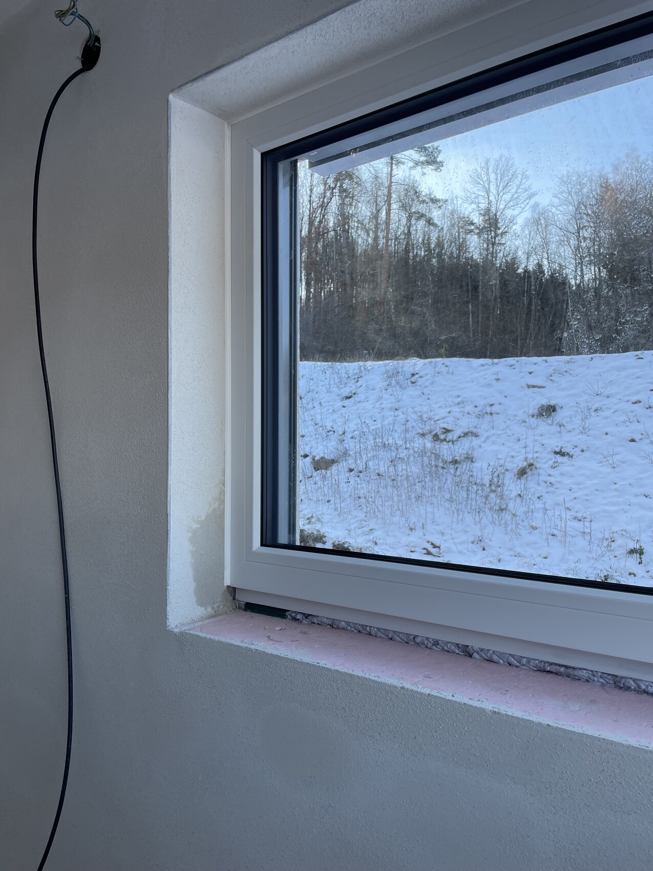 Fenster im Innenraum mit Blick auf eine schneebedeckte Waldlandschaft im Winter