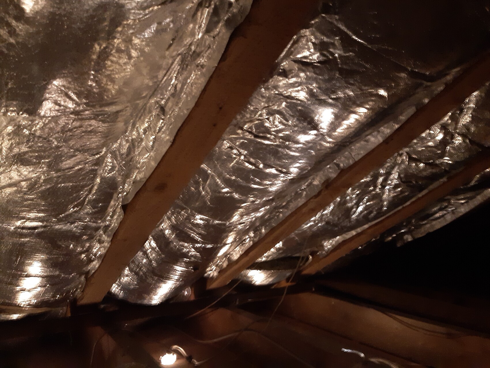 Dachboden mit silberner Folienisolierung und Holzbalken