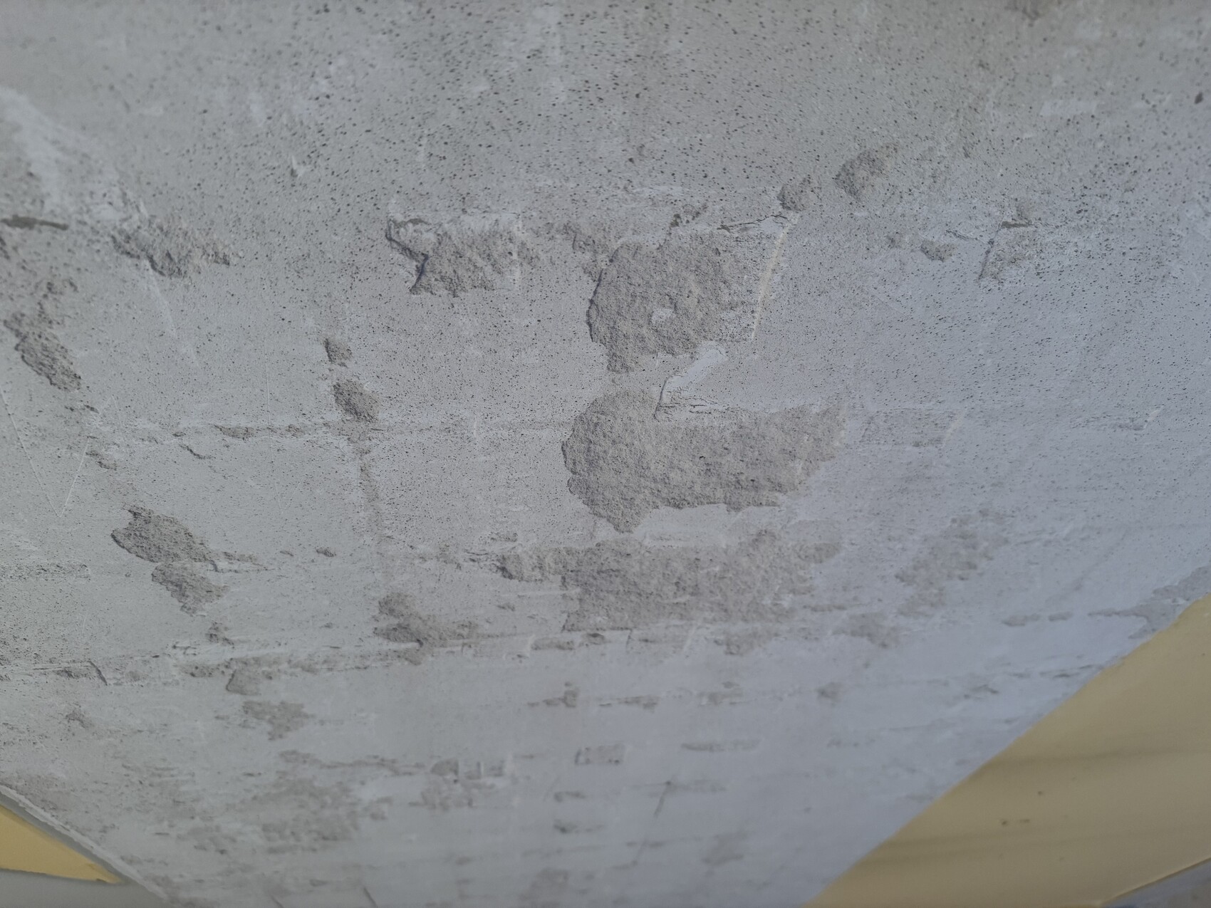 Nahaufnahme einer rauen Betonwand mit abgeplatztem Putz und unregelmäßiger Oberfläche.