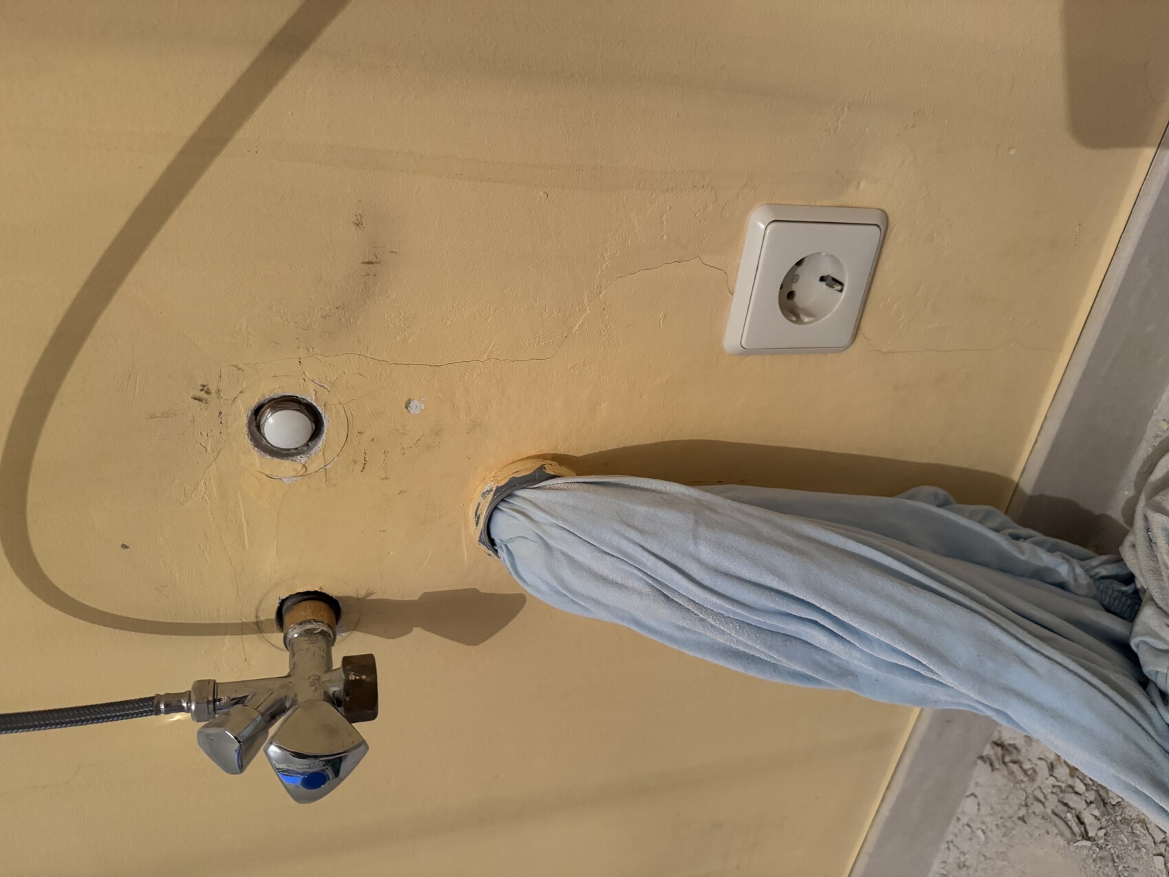 Offene Sanitärinstallation im Bad mit Armatur, Steckdose und Wandrisse.