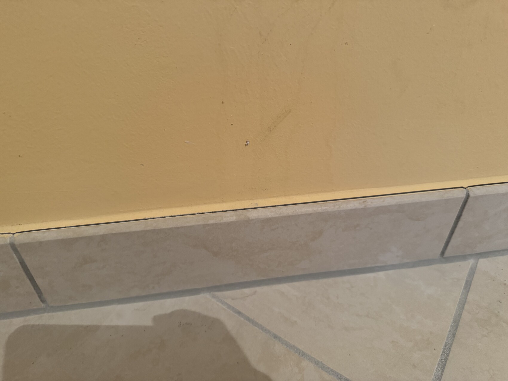 Gelbe Innenwand über beigefarbenen Bodenfliesen mit Kante und Kratzern.