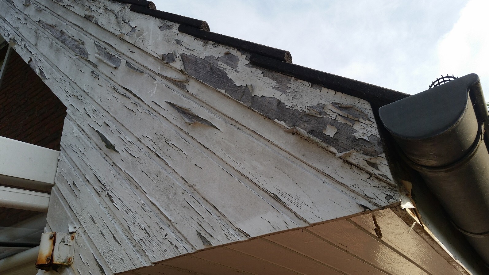 Außenwand mit abgeblätterter Farbe und beschädigter Holzverkleidung am Dachüberstand