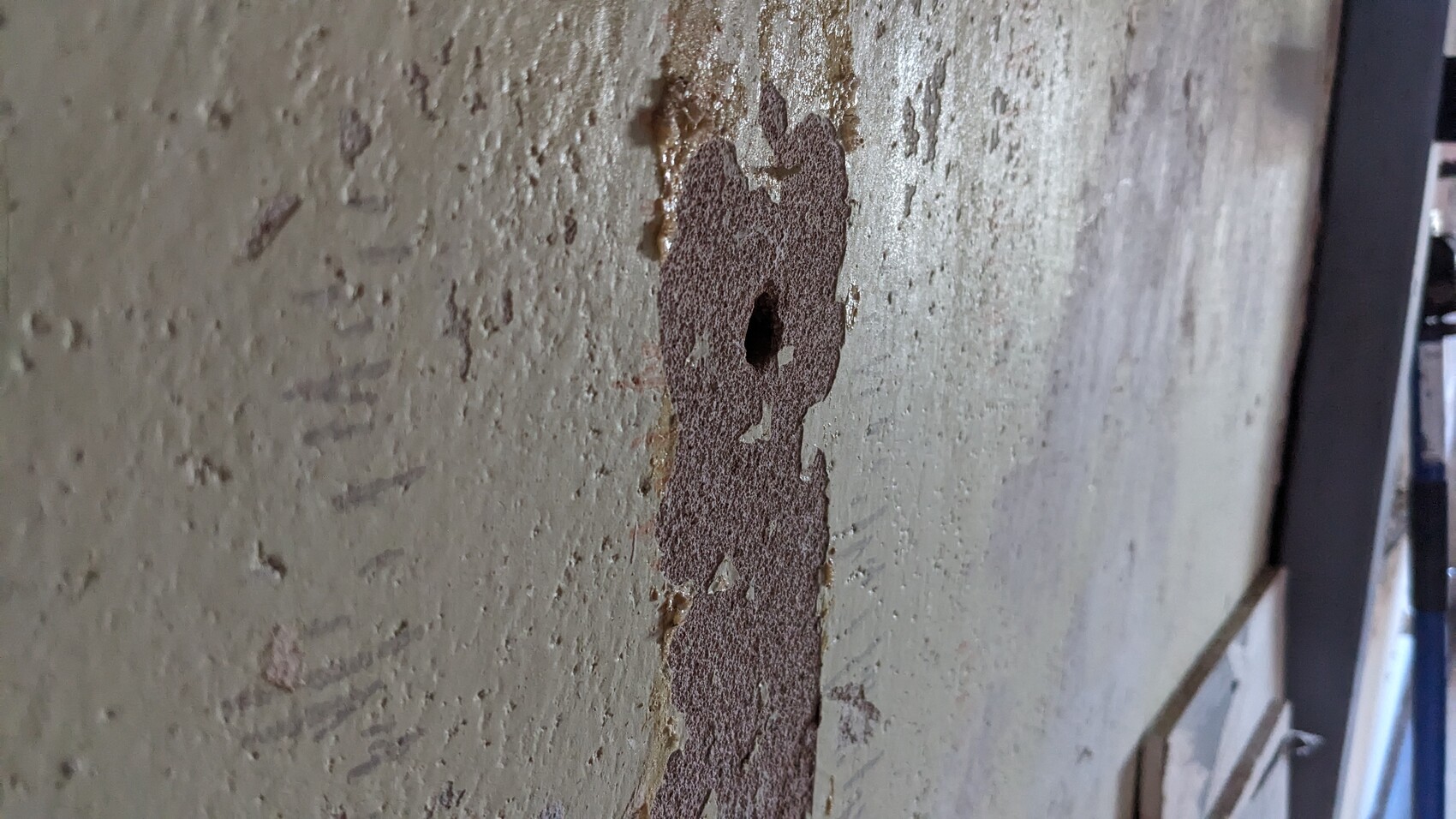 Nahaufnahme einer rauen Wand mit rostigem, vertikalem Streifen und Loch in der Mitte.
