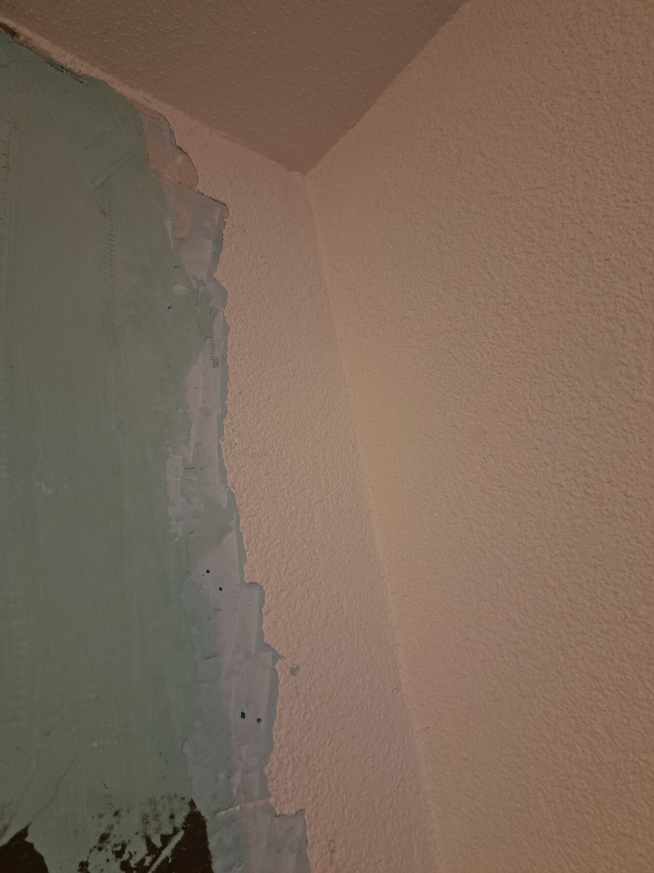 Wand-Ecke: links grün abblätternde Farbe über Putz, rechts pfirsichfarbene, grob strukturierte Wand.