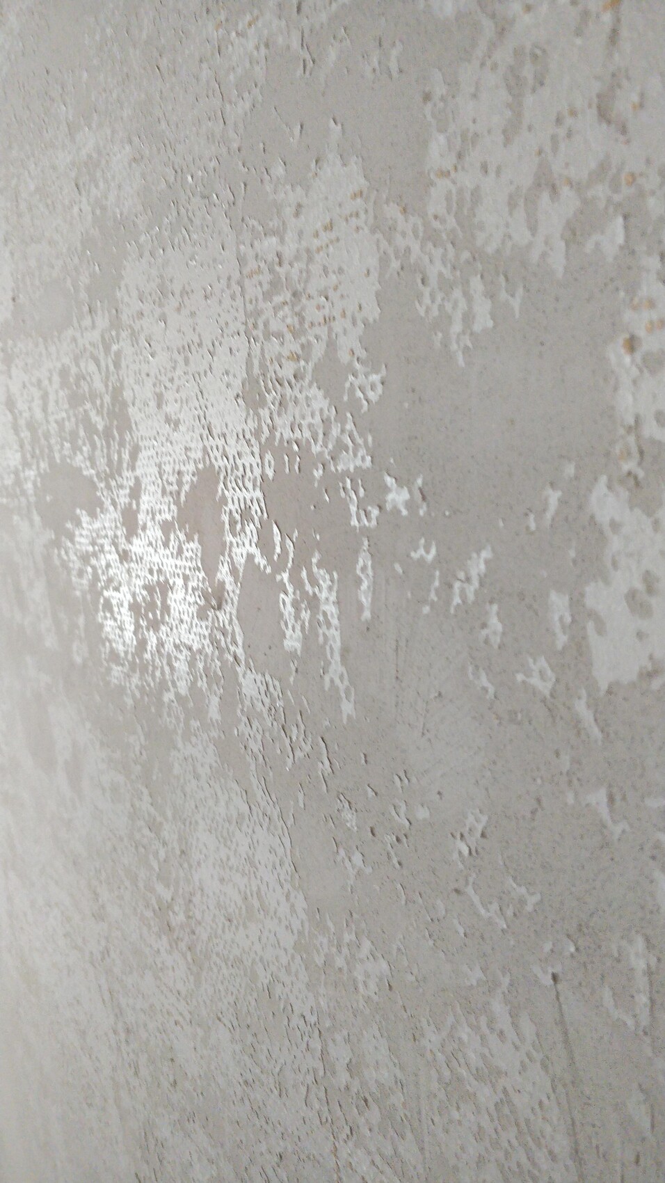 Nahaufnahme einer verputzten Wand mit abblätternder, heller grauer Putzoberfläche.