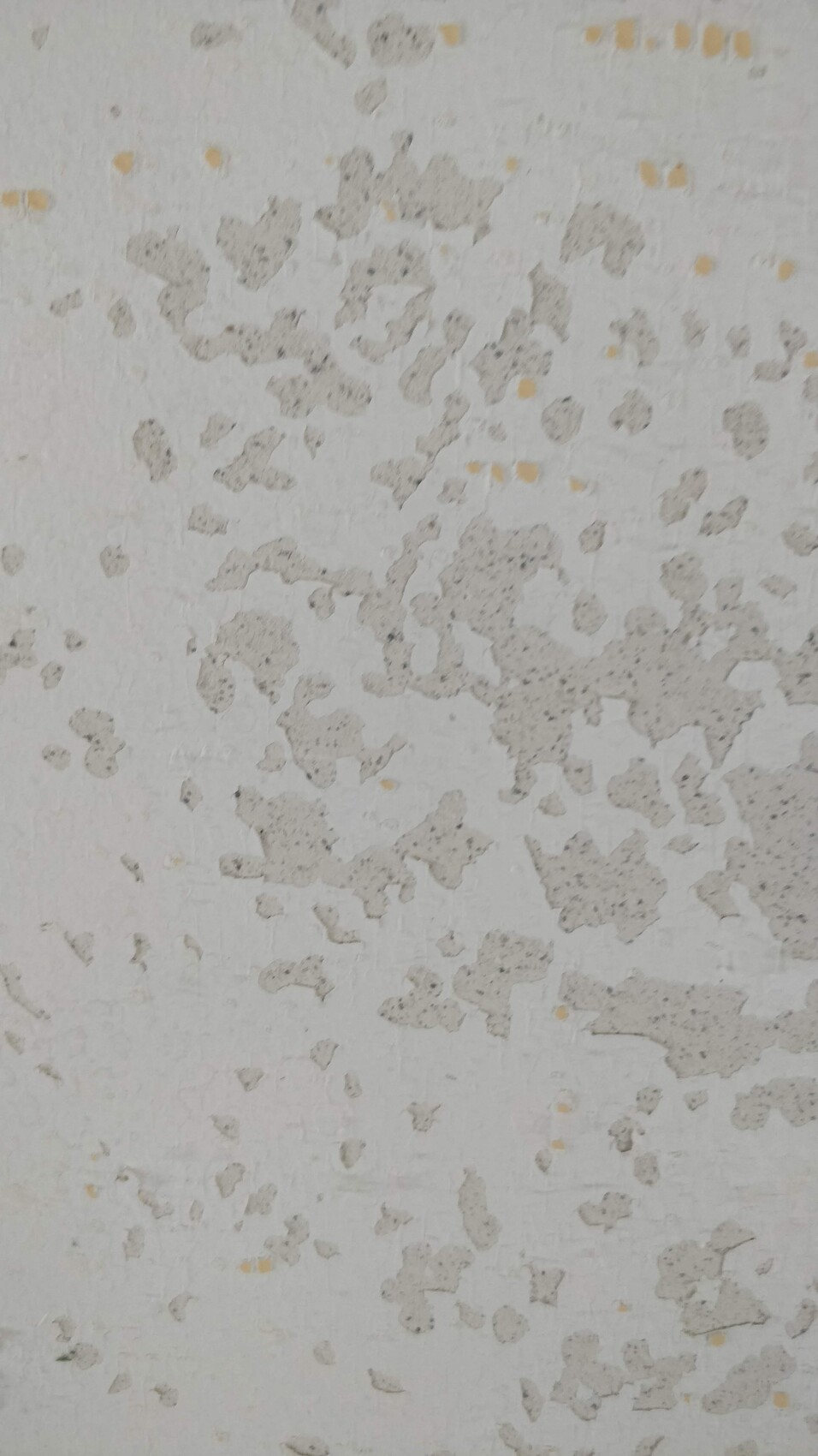 Weiße Wand mit abblätterndem Putz, grauen Flecken und gelben Punkten.
