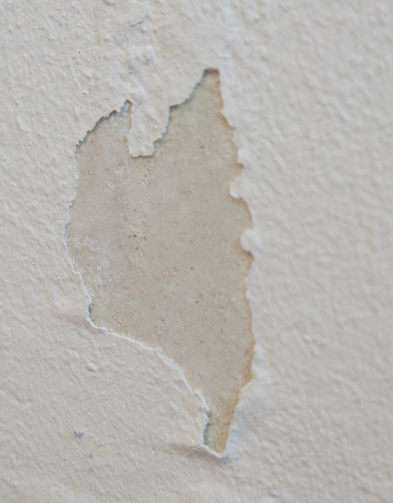 Nahaufnahme einer Wand mit abblätternder Beigefarbe und rauer Oberfläche