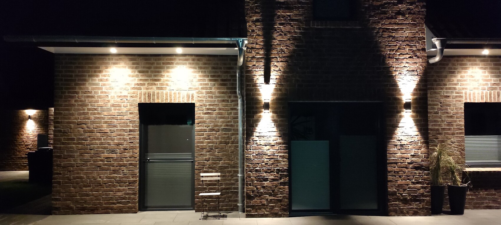 Nachtaufnahme einer Backstein-Fassade mit Türen und Außenleuchten.