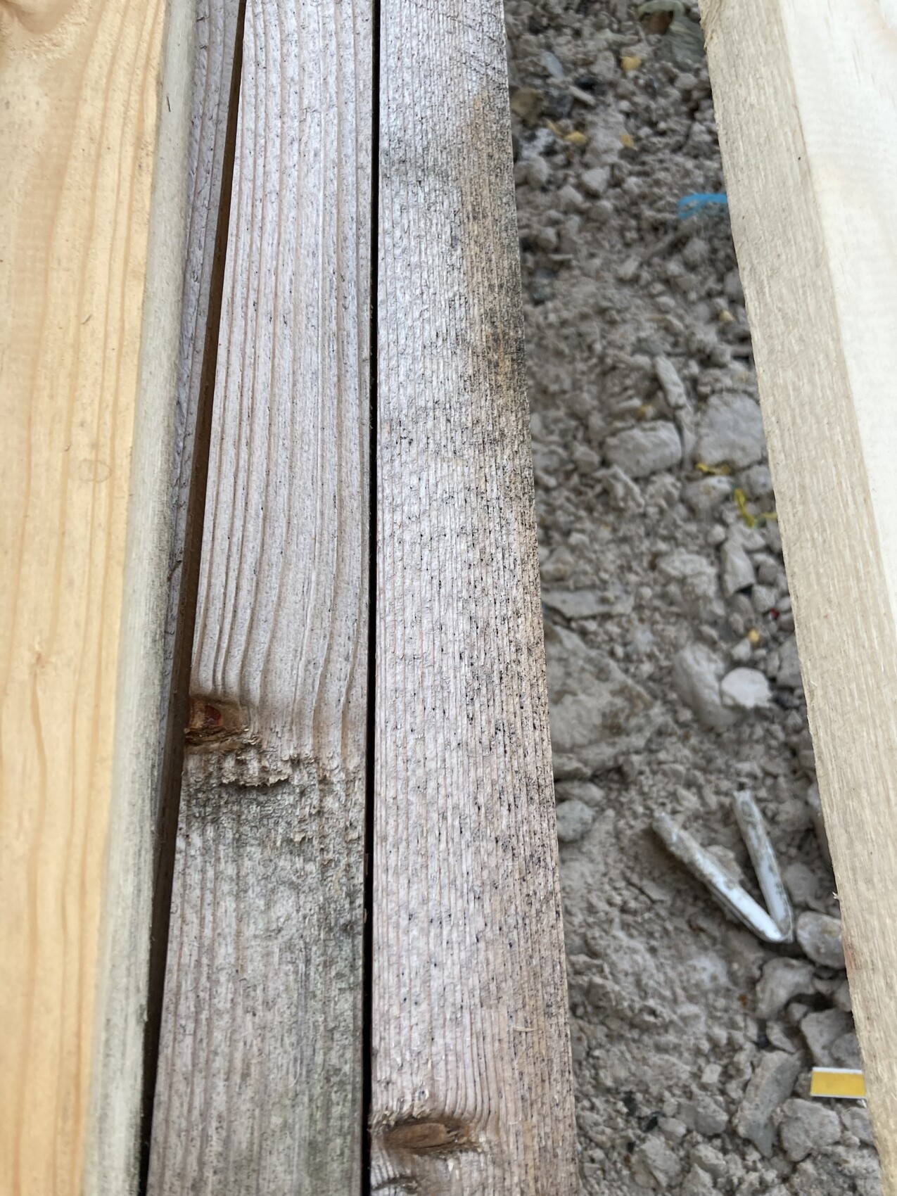 Mehrere Holzlatten liegen nebeneinander auf einer Baustelle, neben Erde und Kies.