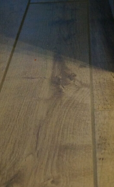 Holzoptik-Fliesenboden mit dunkler Fleckenstelle in der Mitte des Bodens.