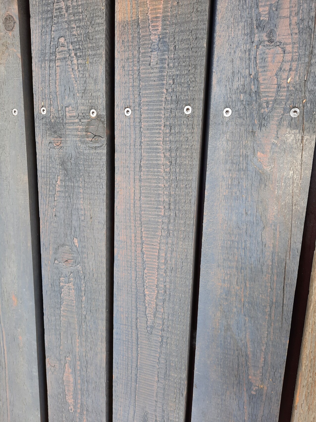 Mehrere vertikale, verwitterte Holzplanken in Blau-Grau mit silbernen Schrauben.