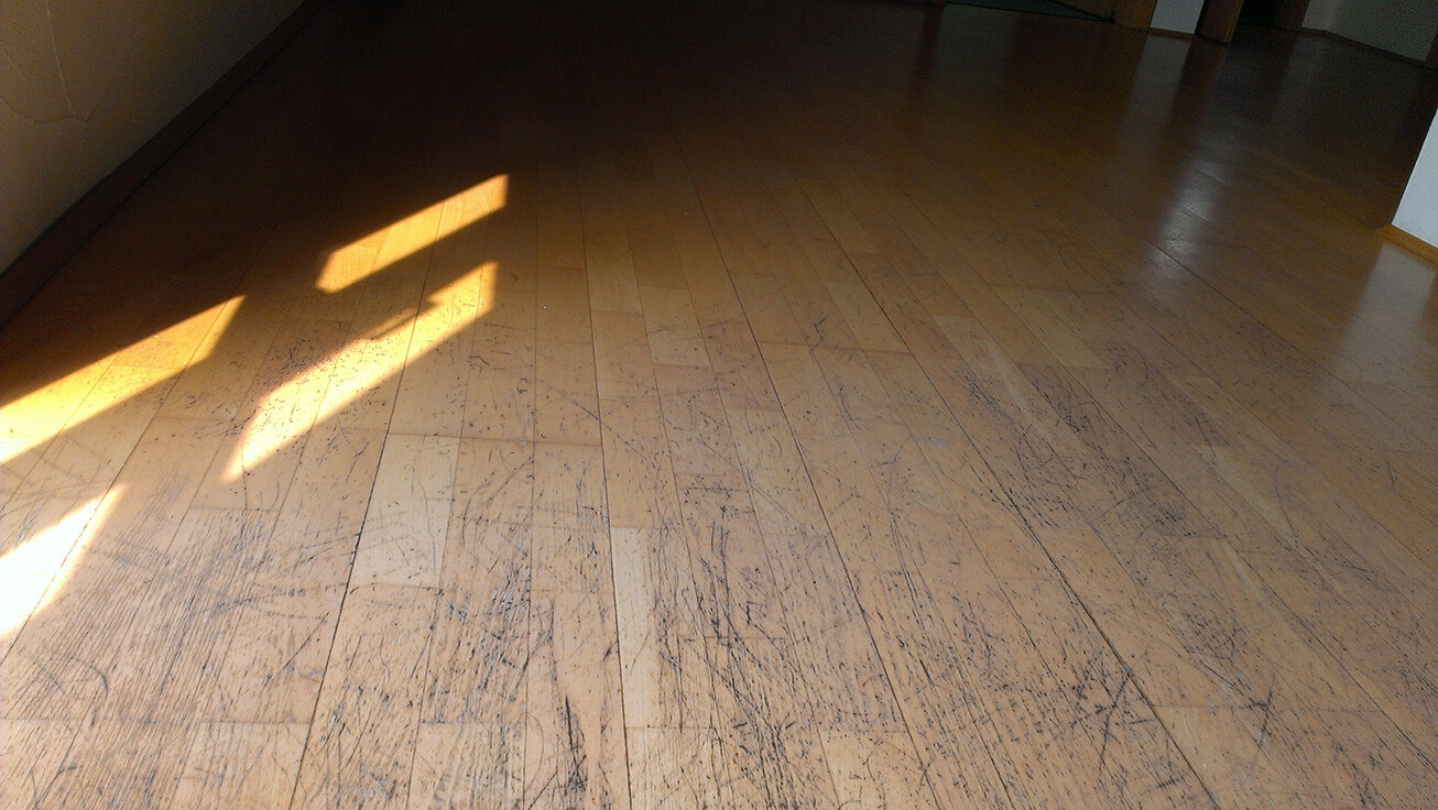 Holzboden mit vielen Kratzern und Sonnenlichtstrahlen im Raum