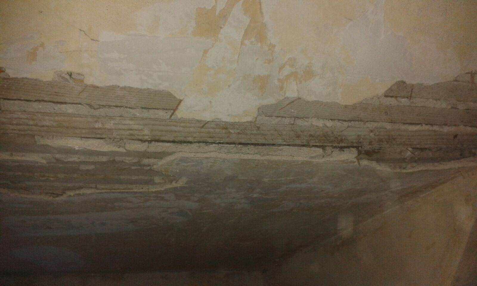 Abgeplatzter Putz an Innenwand mit sichtbaren Schichten und Rissen.