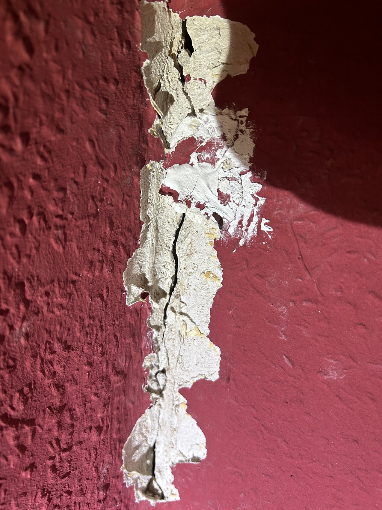 Nahaufnahme einer roten Wand mit abplatzendem Putz und Rissen