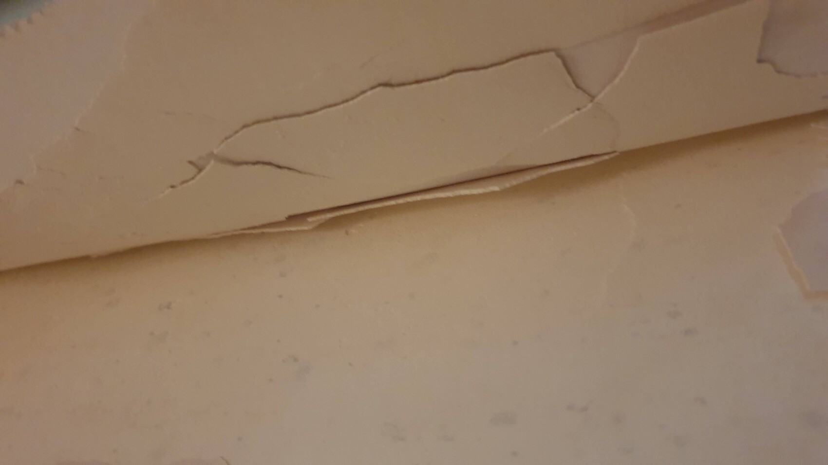 Nahaufnahme einer beige gestrichenen Wand mit abgeblättertem Putz und Rissen.