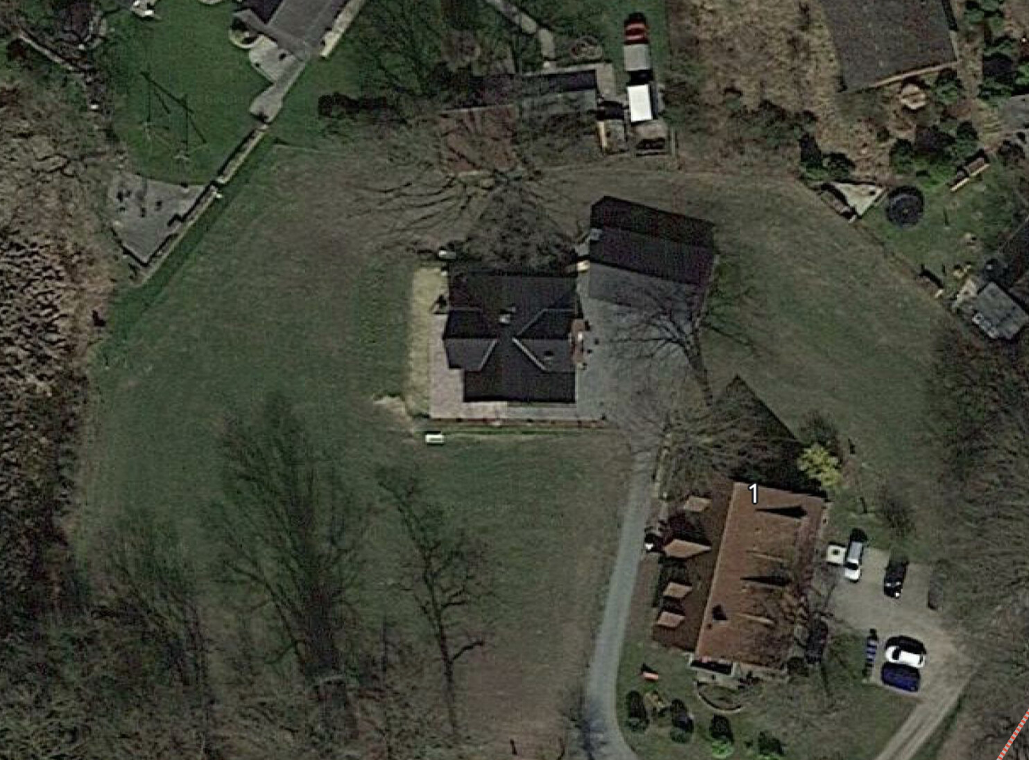 Luftbild eines Einfamilienhauses mit Garten, Zufahrt und Nebengebäuden, von Bäumen umgeben.