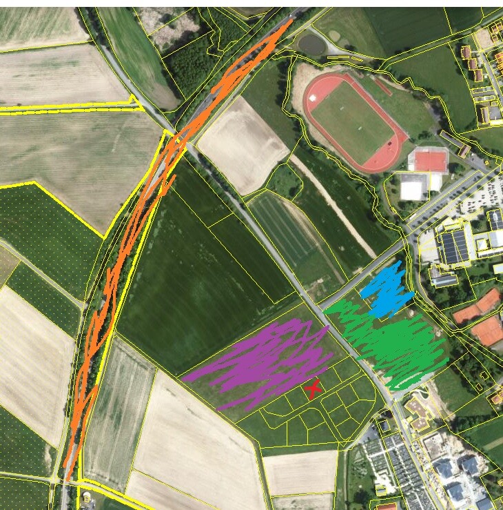 Luftbild von Feldern mit gelben Parzellengrenzen, orange Straße, Sportfeld rechts.