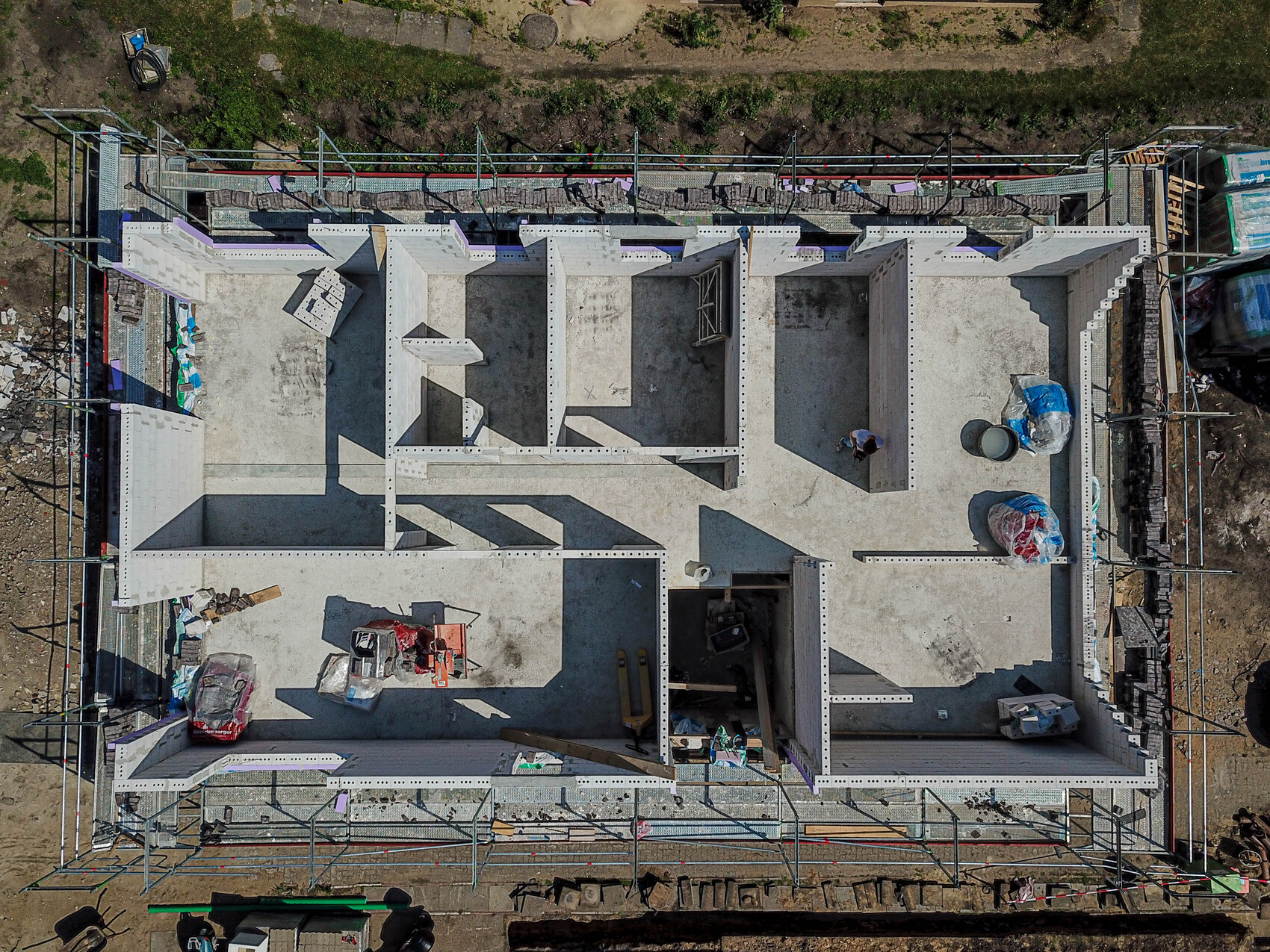 Vogelperspektive eines unfertigen Betonbaus mit Innenwänden, Gerüst und Baustoffen