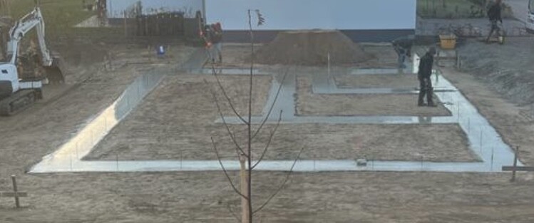 Baustelle mit labyrinthartigen Betonwegen, Baum im Vordergrund, Bauarbeiter im Hintergrund.