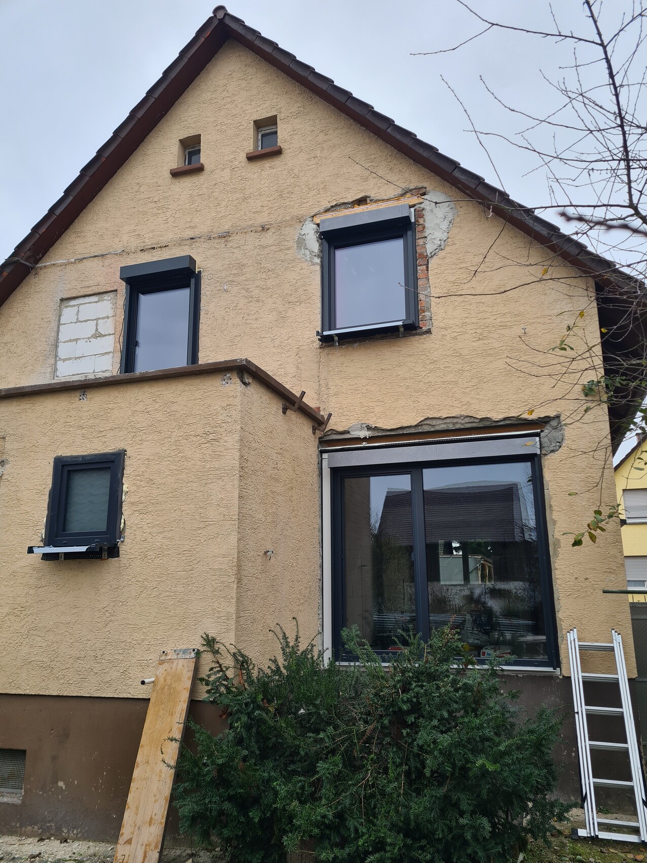 Zweistöckiges Haus mit gelber Fassade, großen Fenstern, Baugeräten und Leiter davor.